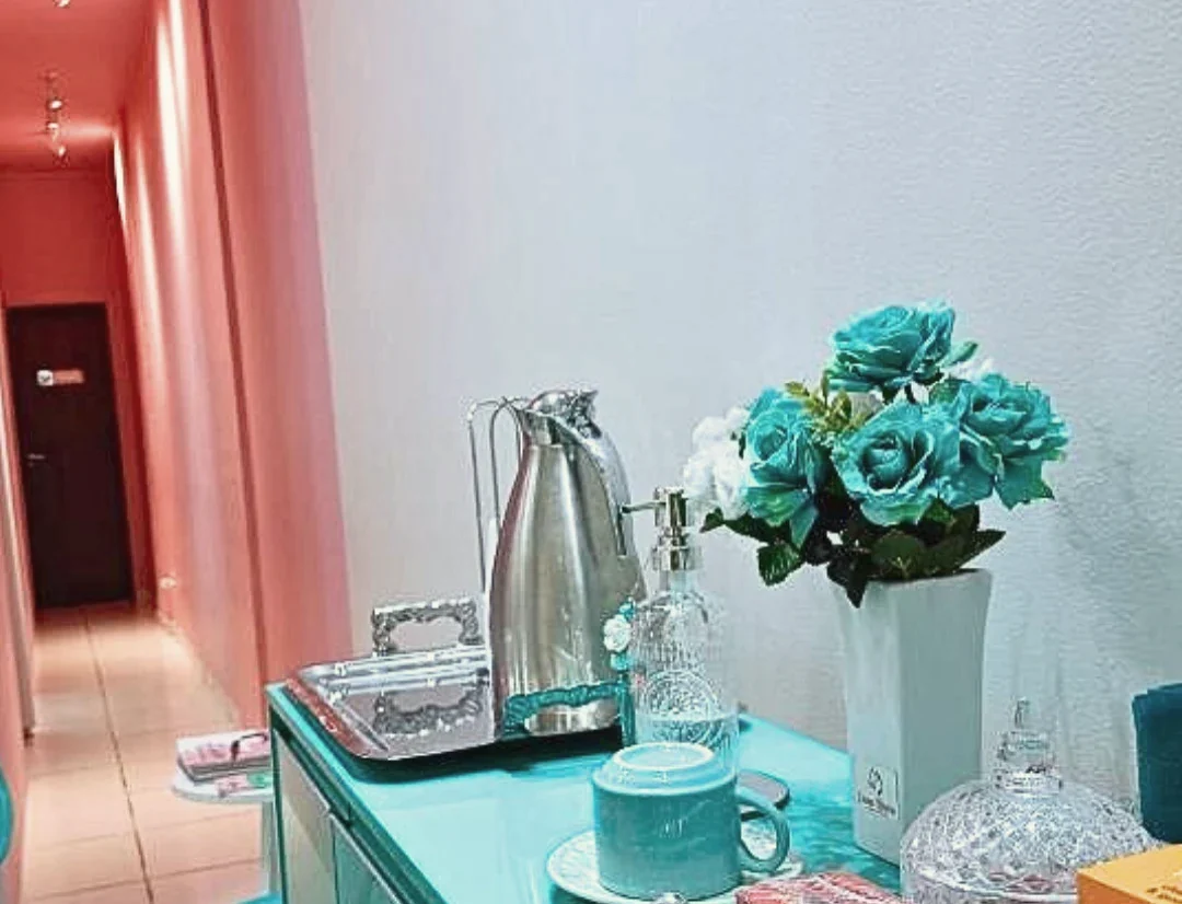 Bancada turquesa da clínica com garrafa térmica, xícara, vaso de flores turquesa e, ao fundo, o corredor de parede coral